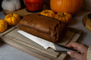Global bread knife next to pumpkin bread on wooden chopping board with pumpkin decorations.