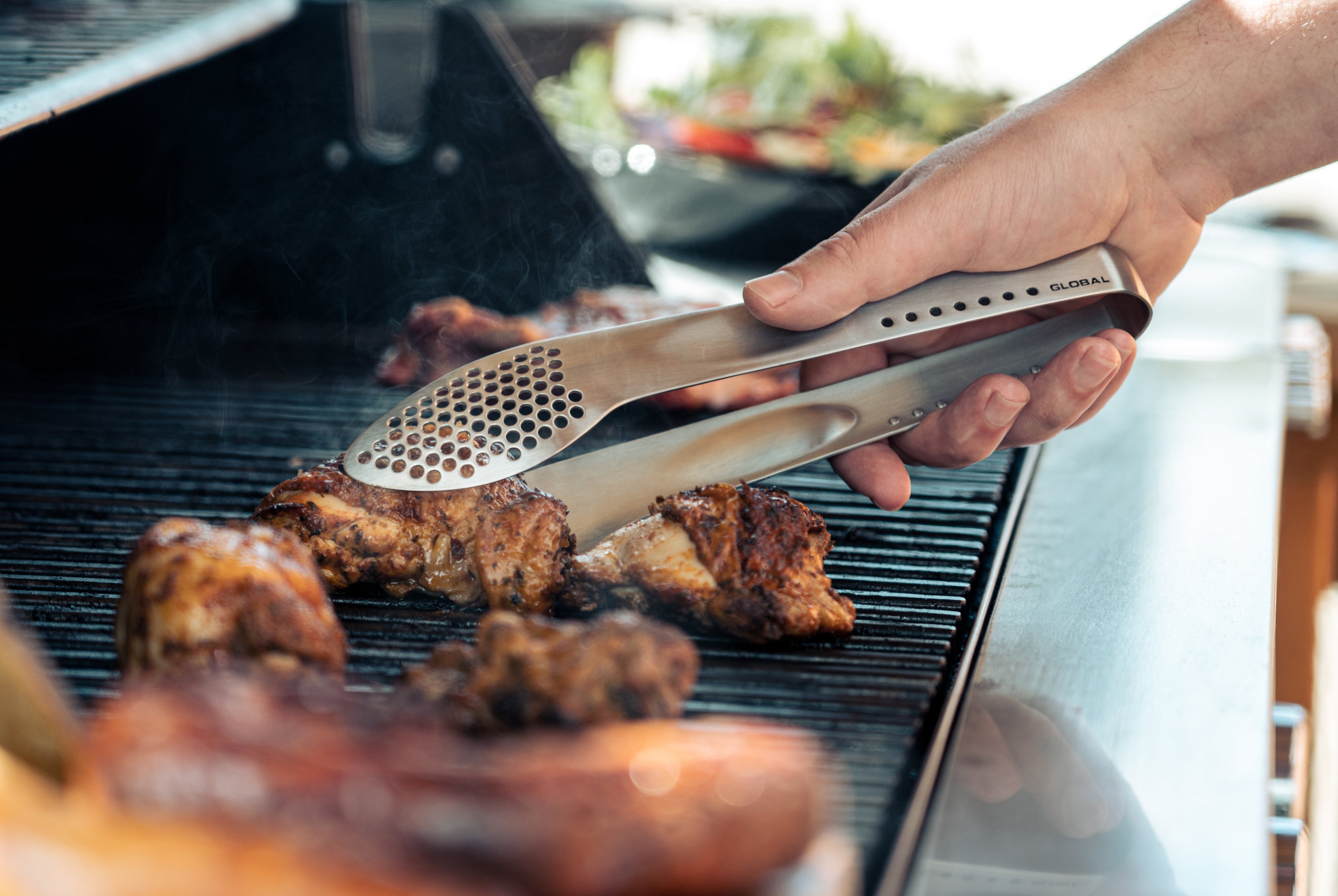 Global kitchen tongs used for grilling meat on the bbq  by barbeque chef. Stainless steel bbq tongs for outdoor cooking and grilling.