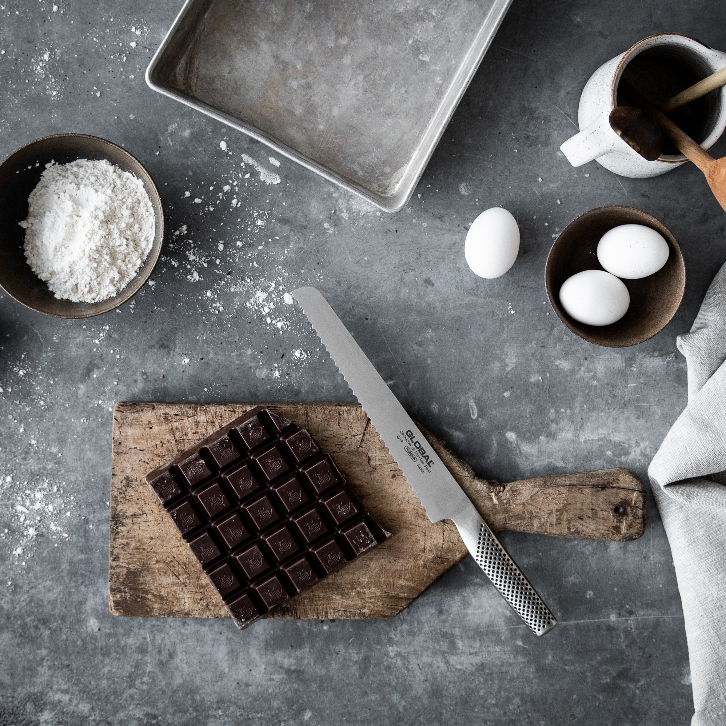 GLOBAL serrated bread knife next to baking set up with chocolate, eggs and baking tray.