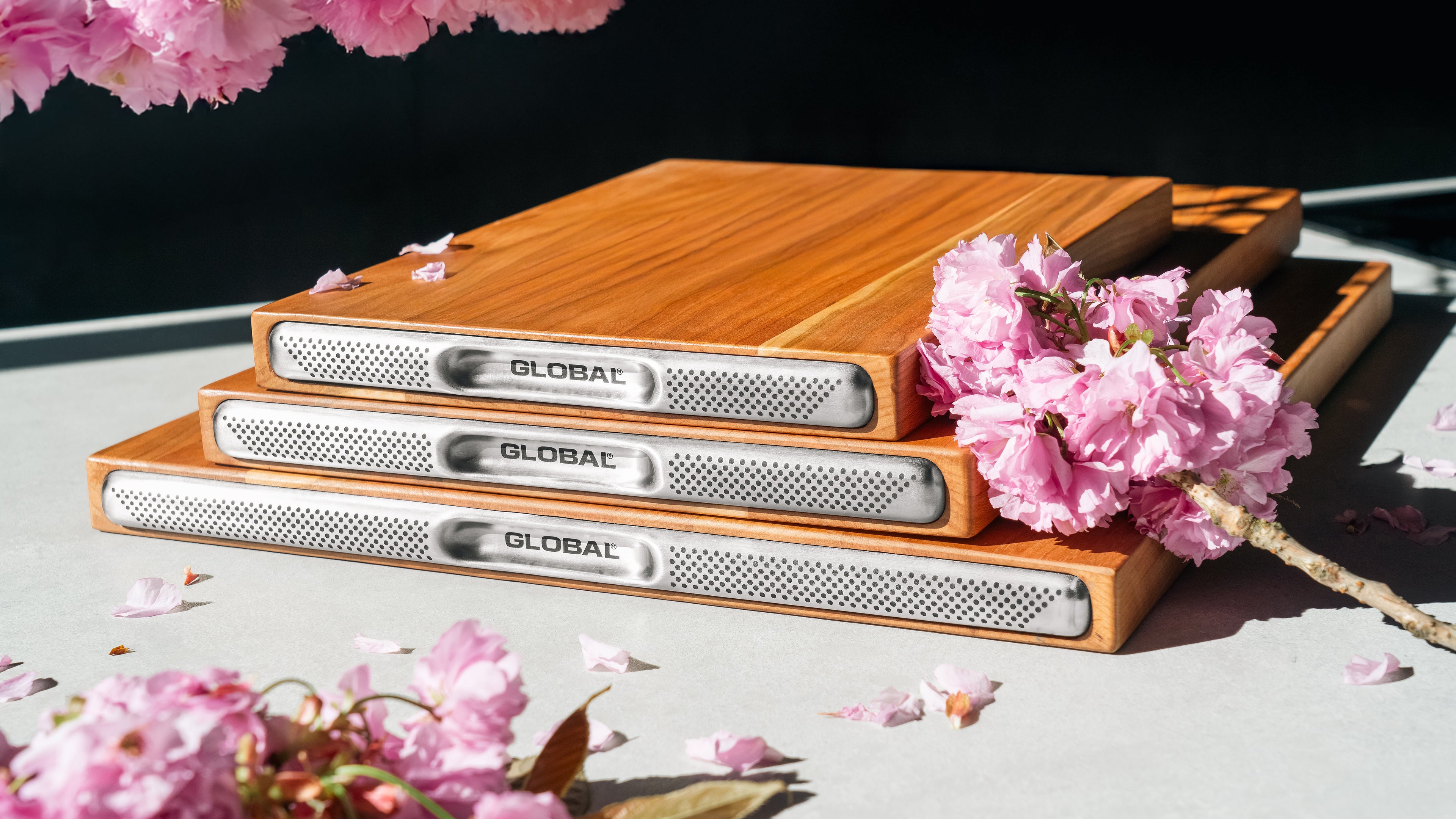 3 premium Global cherry wood chopping boards for professional kitchen prep. Cherry wood cutting boards stacked on top of each other with visible natural wood grain finish on top of kitchen counter for food preparation.