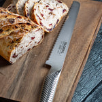 Sliced bread on a wooden cutting board with a Global serrated bread knife. Large stainless steel bread knife.