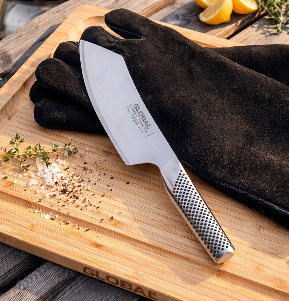 BBQ Knife on a bamboo wooden cutting board with leather BBQ gloves, lemon, and herbs.
