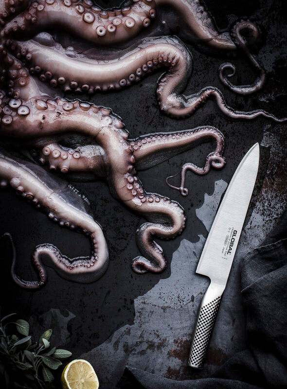 Global G-2 chefs knife next to lemon and octopus tentacles. Professional stainless steel kitchen knife for chefs, seafood and culinary food prep.