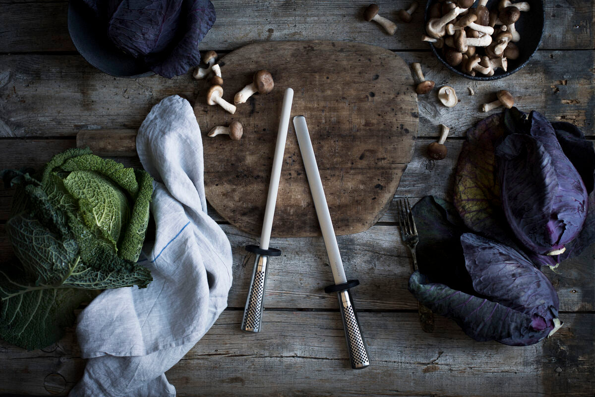 2 GLOBAL Sharpening steels on wooden background surface with cabbages and mushrooms.