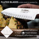 Global chef's knife cutting pineapple with text about fluted blades benefits. Fluted blades create small air pockets for reduced food adhesion, improved food release and smooth, effortless cuts.