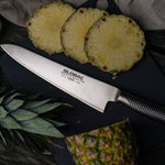 Sliced pineapple with a Global stainless steel chef's knife (G-16) on a dark surface