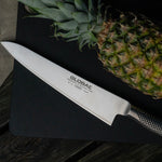Large Global chef's knife with a pineapple on a dark surface. Stainless steel cook's knife.