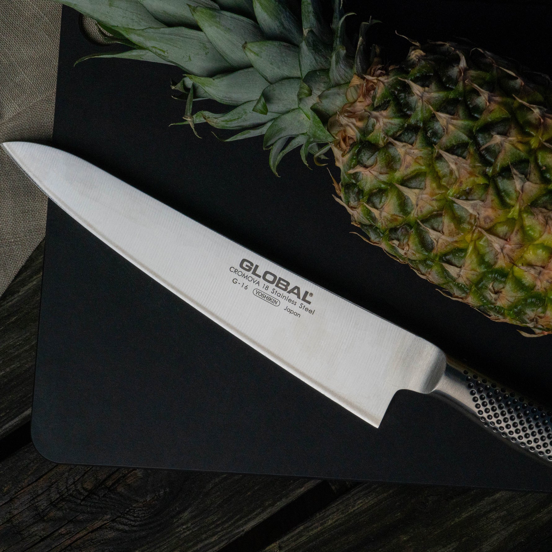 Large Global chef's knife with a pineapple on a dark surface. Stainless steel cook's knife.