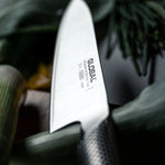 Close-up of a Global G-2 Cook's Knife ultra sharp blade with vegetables in the background for effortlessly cutting vegetables.