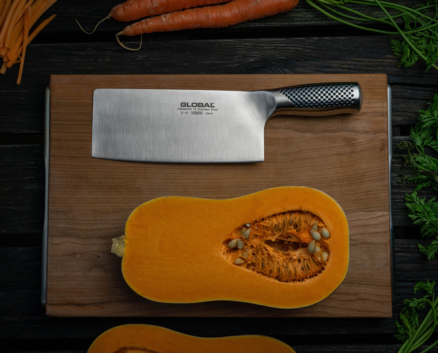 Global Chinese chopping knife beside butternut squash on wooden cutting board.