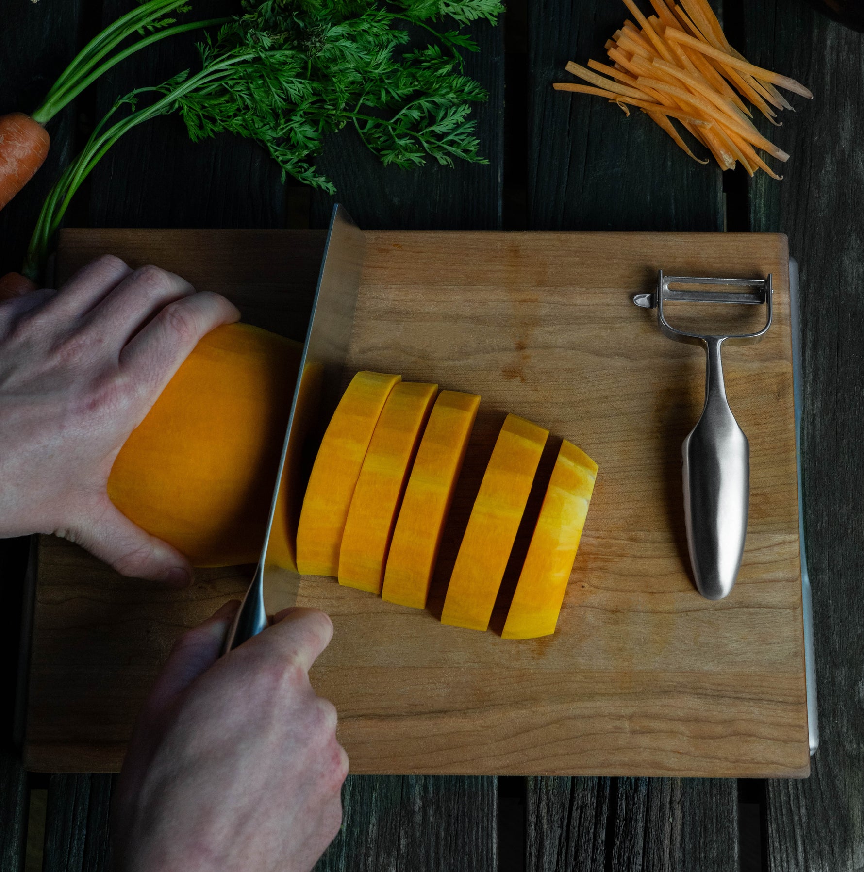Chinese stainless steel chef's knife for chopping vegetables, meat and fish being used by chef to chop butternut squash next to Global vegetable peeler. 