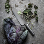 Stainless steel vegetable chopper knife on a stone surface with purple cabbage and green leaves
