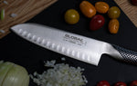 Global santoku chef's knife on a cutting board with vegetables, santoku knife stainless steel.