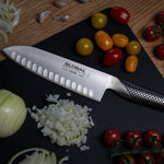 Global Japanese chef's knife on a cutting board with chopped onions and tomatoes, the global G-80 stainless steel santoku knife.