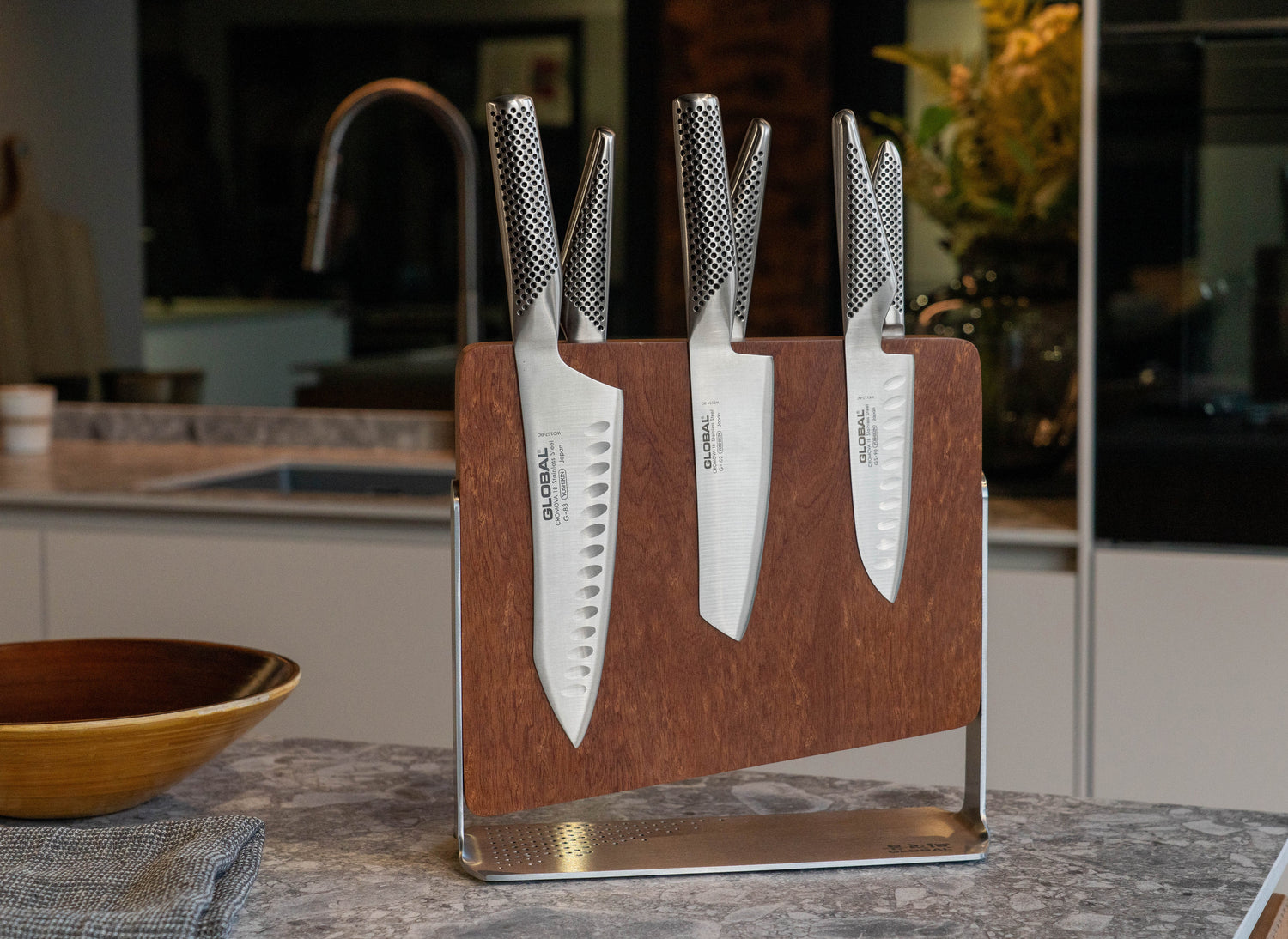 Global set of knives in a wooden block on a kitchen counter. Magnetic wooden knife block with 6 Global knives.