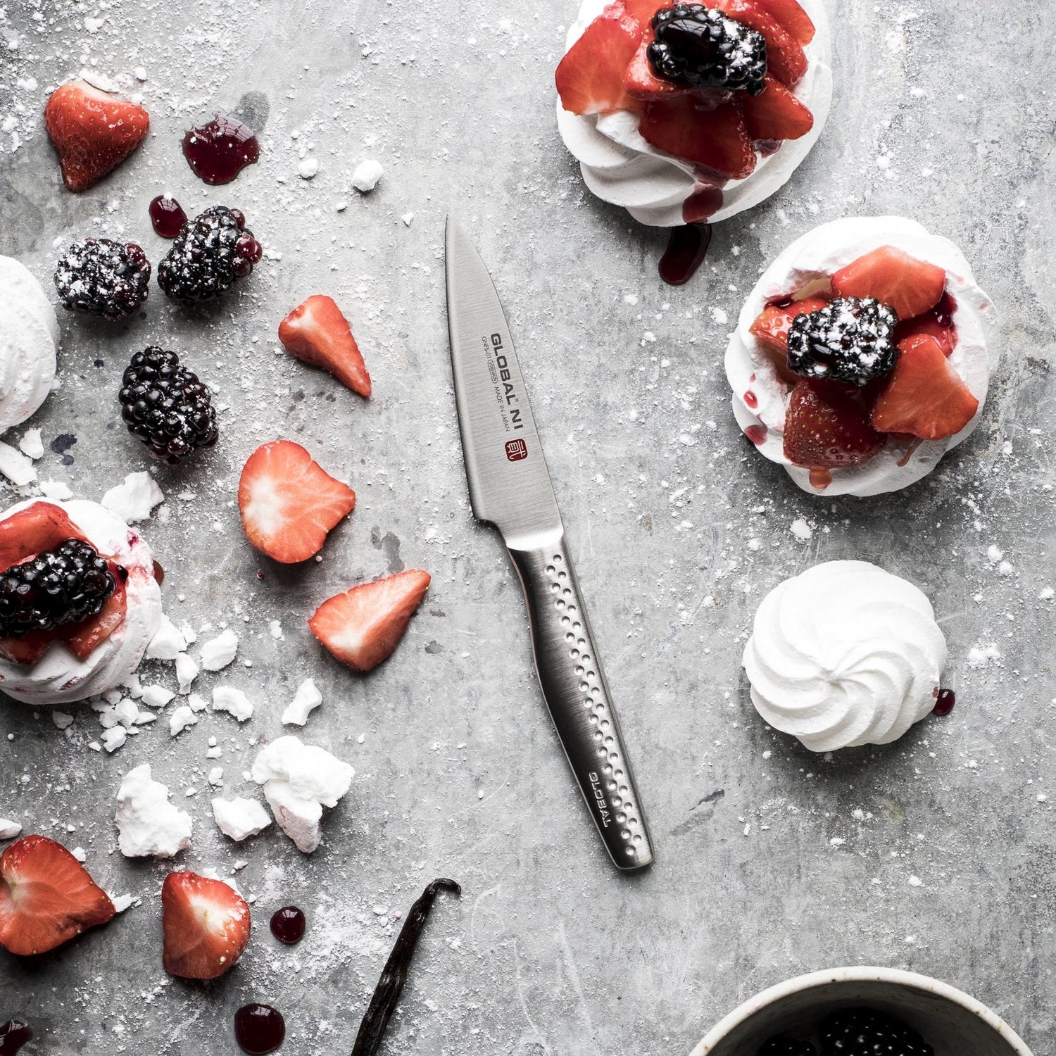 Decorative setting with dessert items, a Global peeling knife, and vanilla beans on a grey surface.