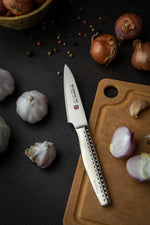 Global Ni paring knife, a stainless steel small kitchen knife on wooden cutting board with garlic and onions.