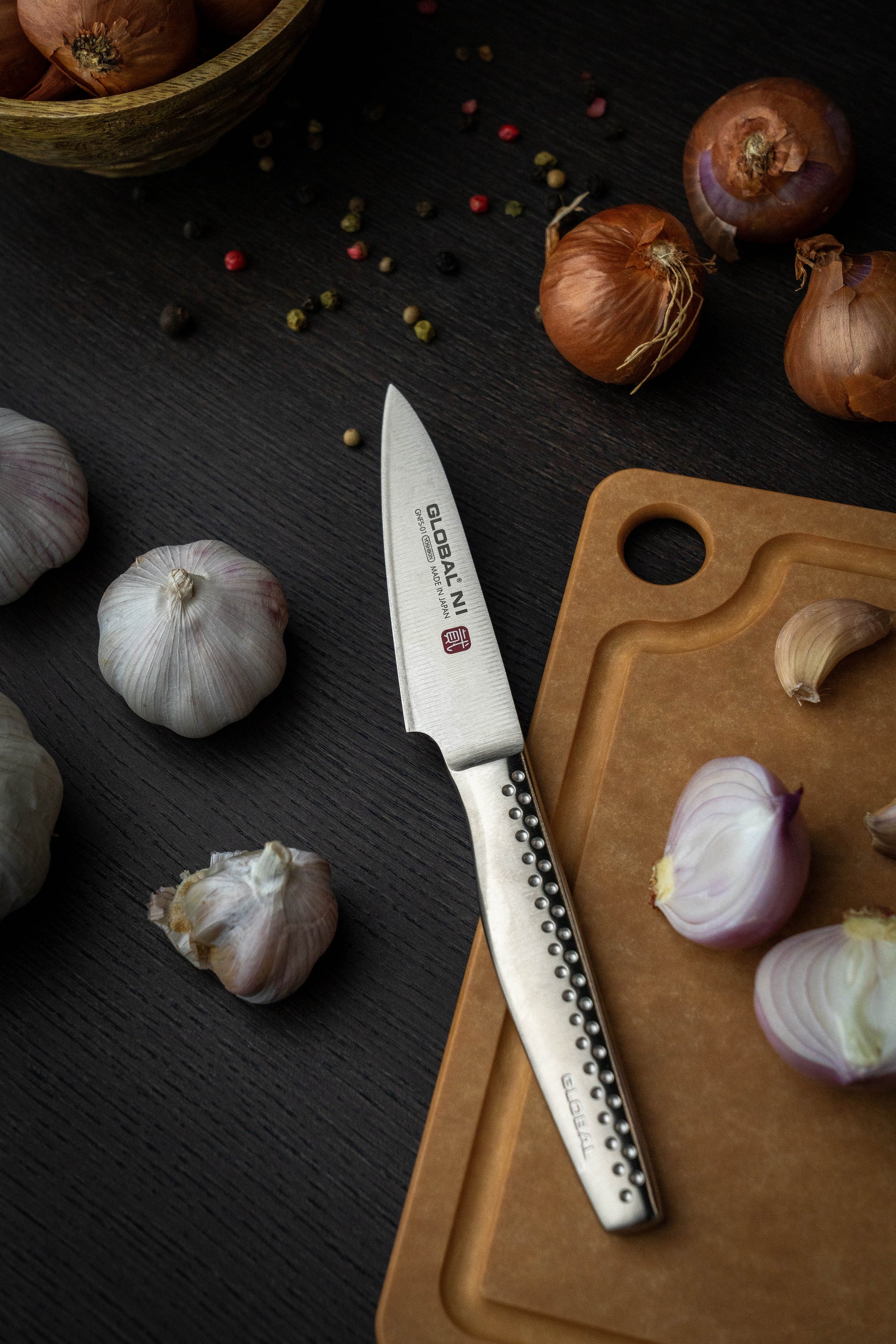 Global Ni paring knife, a stainless steel small kitchen knife on wooden cutting board with garlic and onions.