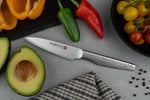 Global kitchen knife on a grey surface with vegetables and an avocado. Small Japanese kitchen knife, Global Ni utility knife.
