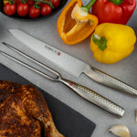 Japanese carving knife and fork set on a cutting board with vegetables and roasted chicken. Global Ni Carving set for slicing meat with control.