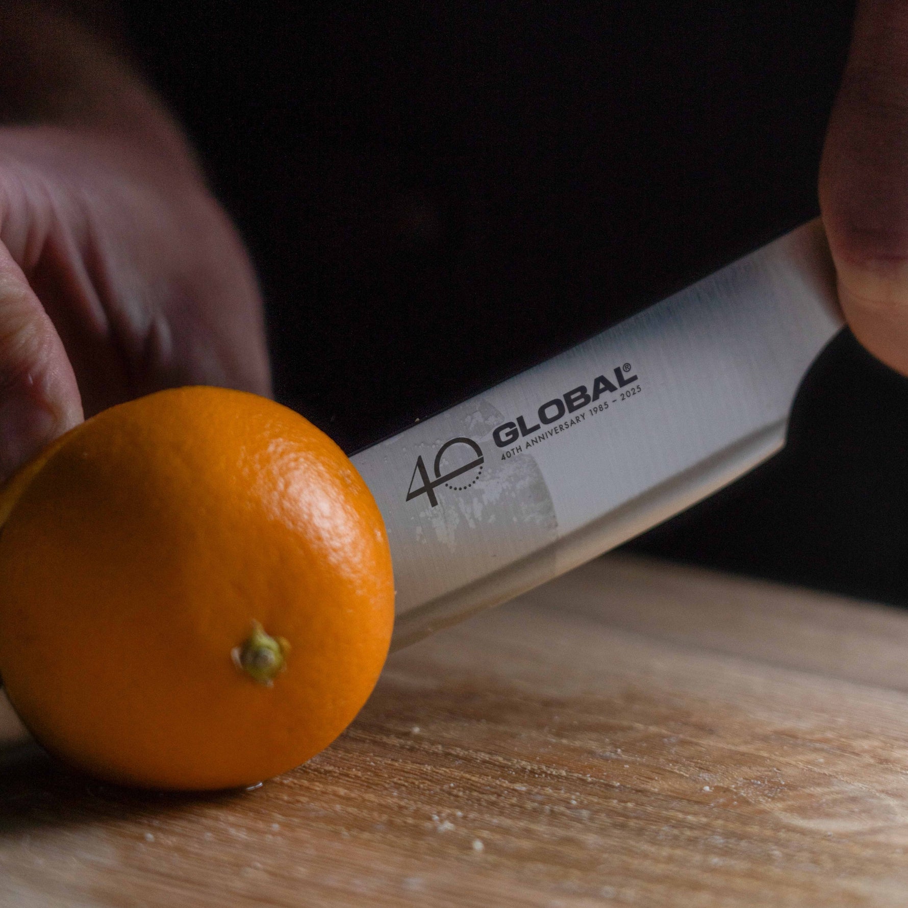 Global stainless steel kitchen knife with Global branding cutting an orange on a wooden surface