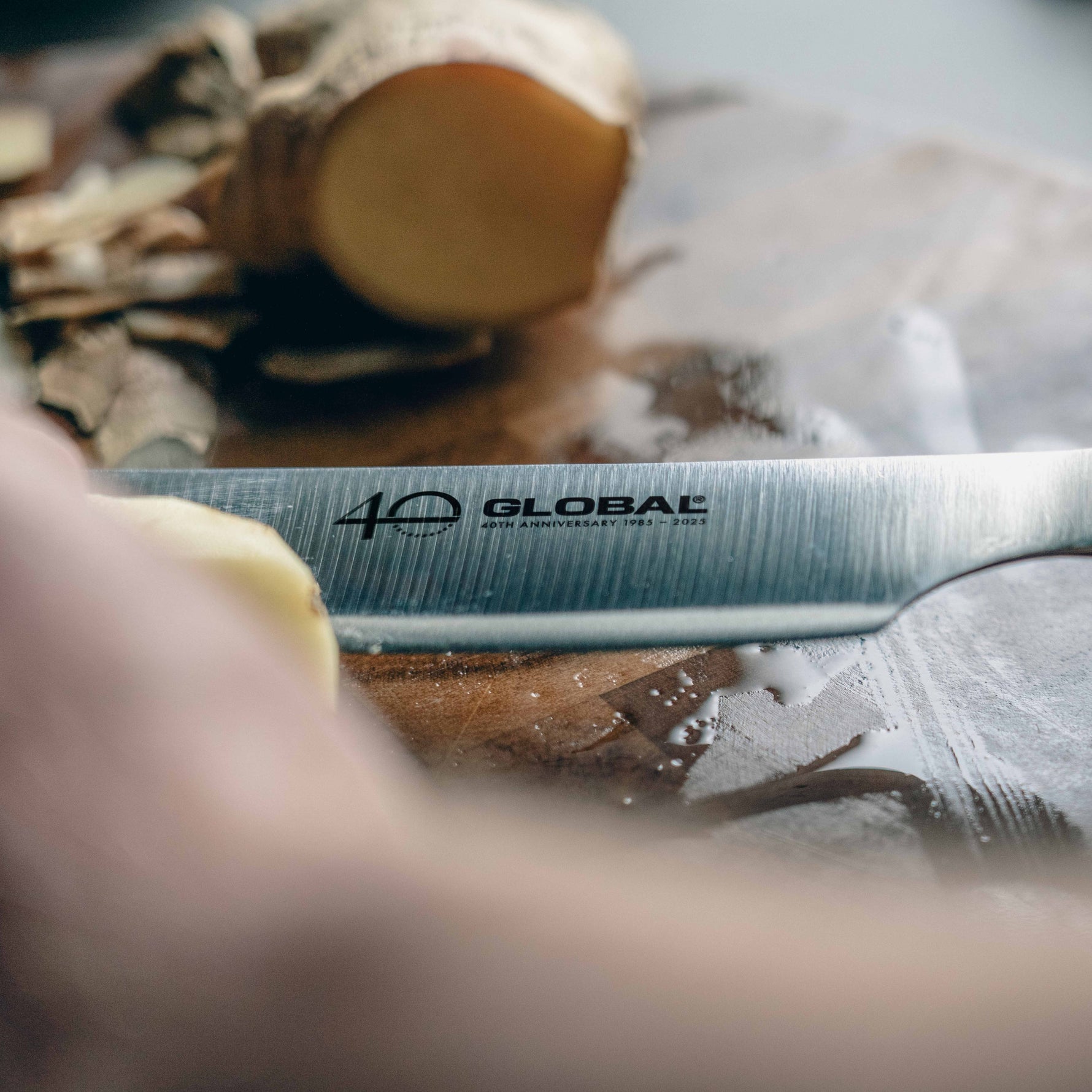 Japanese Stainless Steel Kiritsuke Knife with 'Global' branding cutting a piece of ginger on a wooden board.