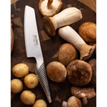 Global vegetable chopper kitchen knife on a wooden surface with mushrooms and potatoes