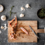 Rawseafood and shrimp on a wooden cutting board with garlic and herbs on a gray surface with Global GSF-15 peeling knife for prepping seafood.
