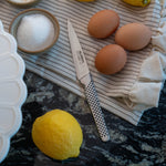 Global stainless steel utility knife, eggs, lemon, and salt on a striped cloth with a dark surface. Utility knife can be used as paring knife,  peeling knife, a versatile kitchen knife.