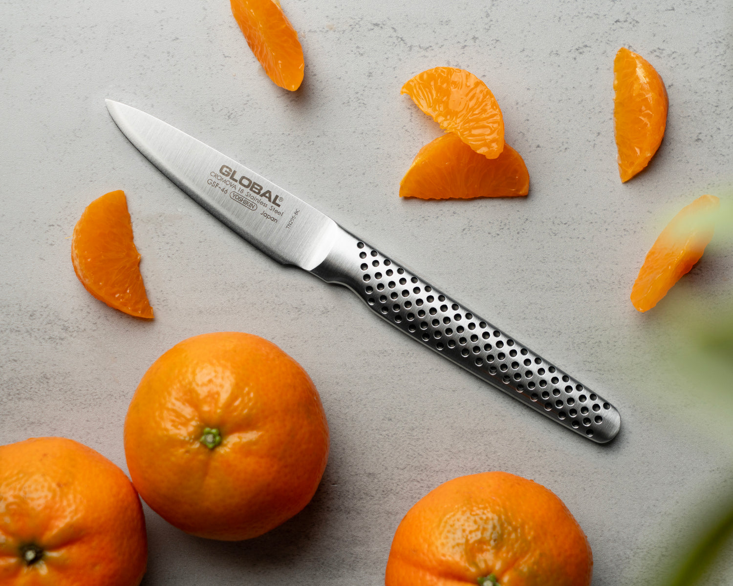 GSF-46 Global peeling knife on a gray surface with sliced oranges. Japanese petty knife for intricate tasks.