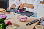 Home cooking using mandolin slicer for cutting onion with finger safety guard for safe and even slicing of onion into thin, uniform pieces.