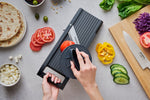 Chef using Global kitchen mandoline vegetable slicer for thinly slicing tomatoes with protective finger guard for safe food prep.