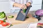 Cooking enthusiast using Global Japanese mandoline for cutting cucumber into thin, even slices on wooden cutting board for healthy meal prep.