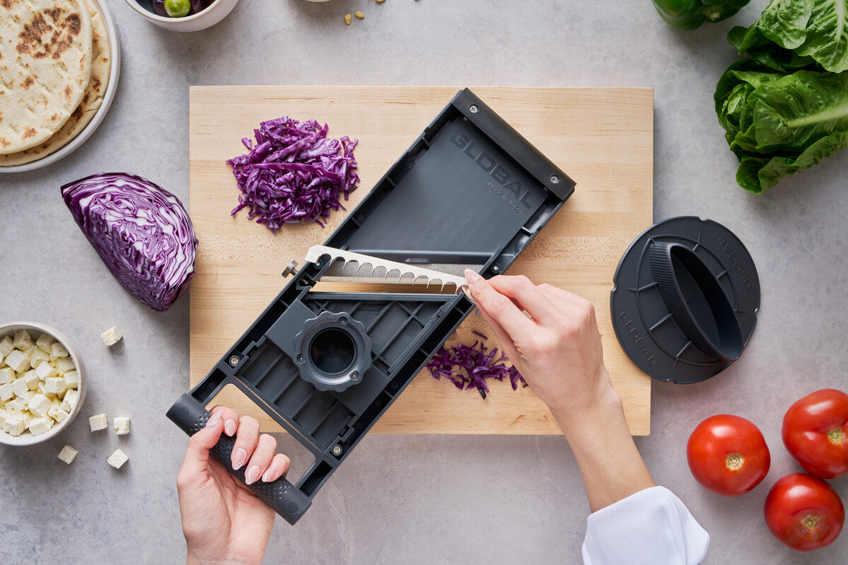 Back view of Global's stainless steel mandolin slicer showing cook easily changing interchangeable blade attachment for julienne cuts of vegetables.