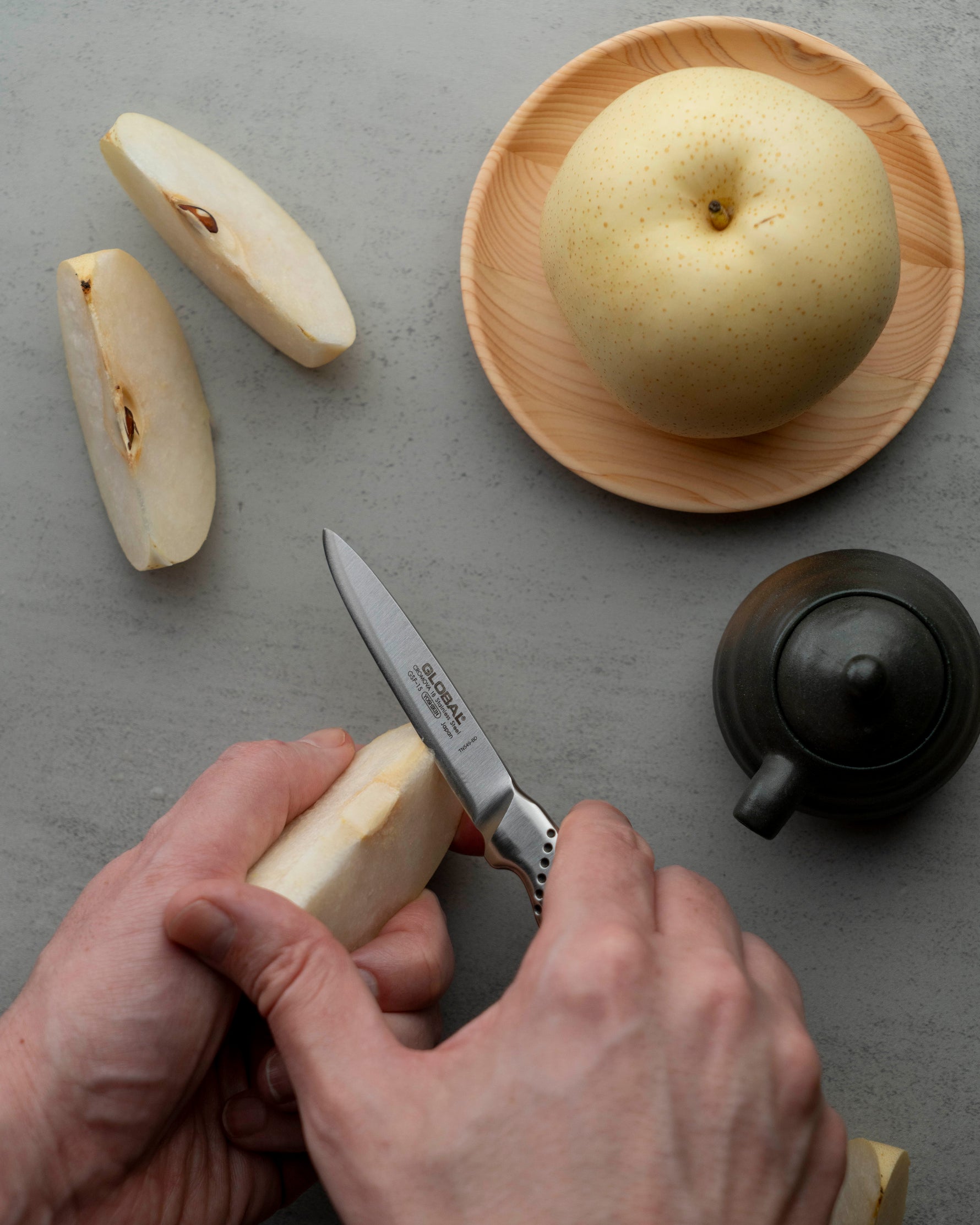 Global peeling knife being used by chef to peel and core apple next to large apple and small pot.