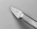 Close-up of a Global utility knife GSF-22 on a grey background. Shows ultra sharp blade with 15 degree cutting edge and ergonomic handle with indentations for a kitchen knife with a comfortable grip.