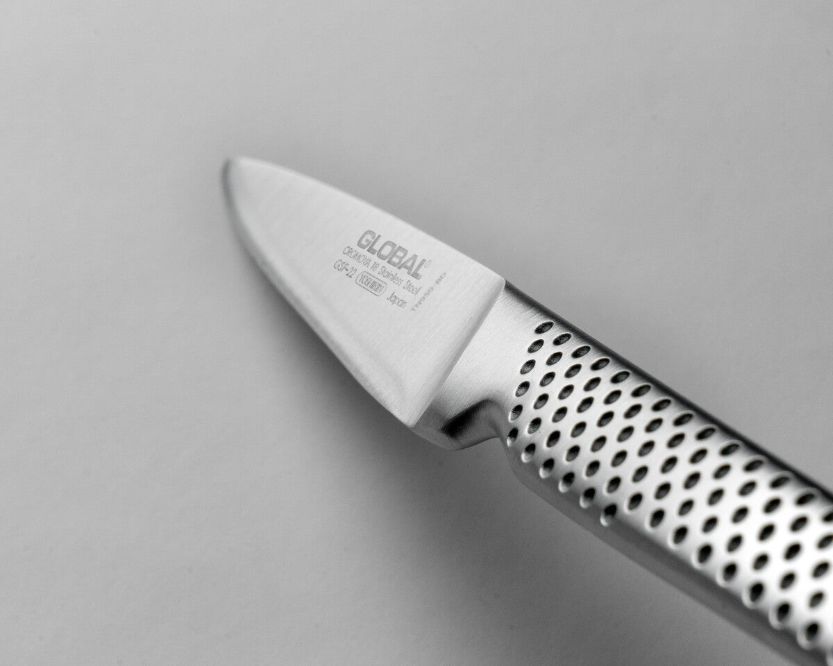 Close-up of a Global utility knife GSF-22 on a grey background. Shows ultra sharp blade with 15 degree cutting edge and ergonomic handle with indentations for a kitchen knife with a comfortable grip.