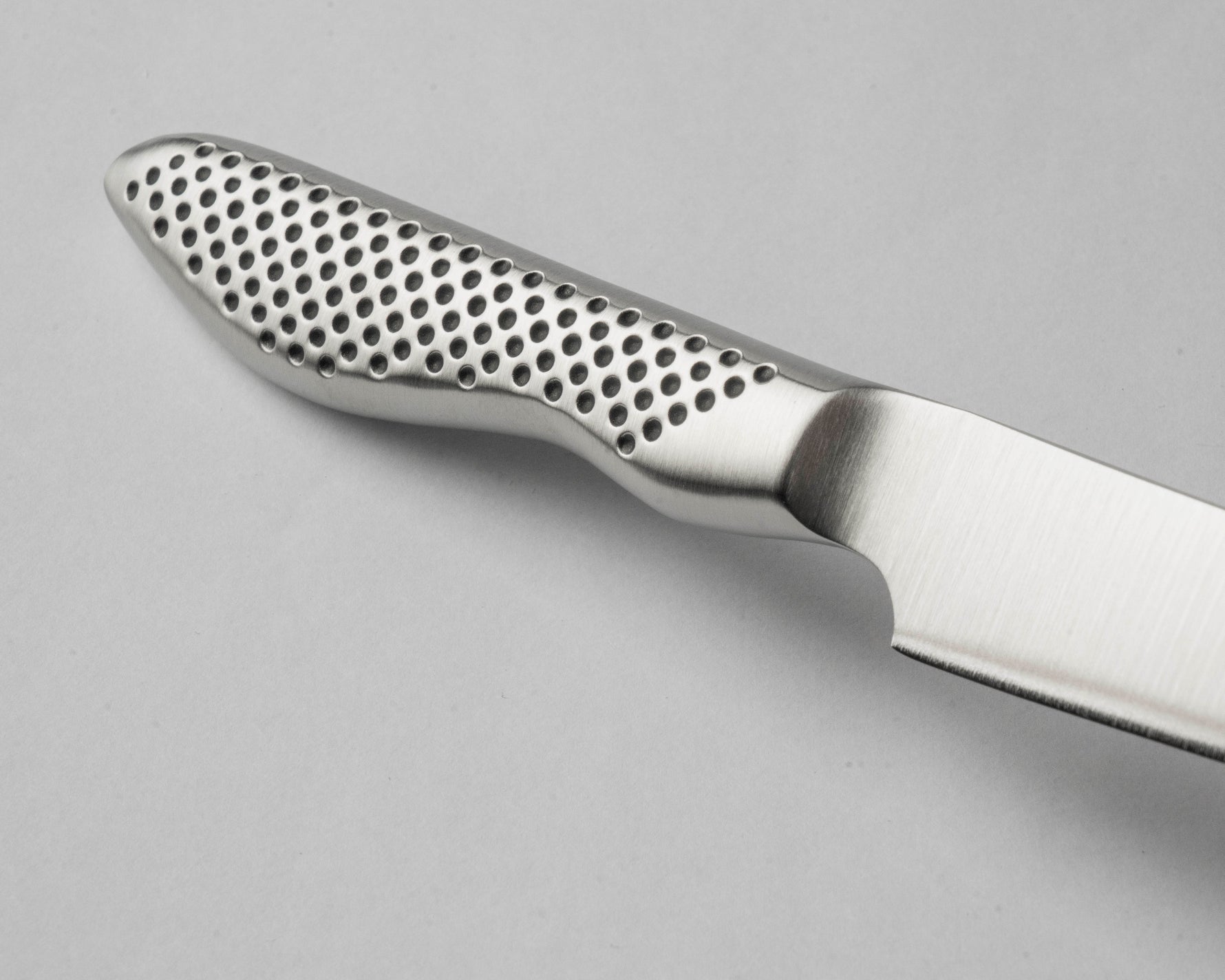 Close-up of a global paring knife handle with a textured pattern on a gray background