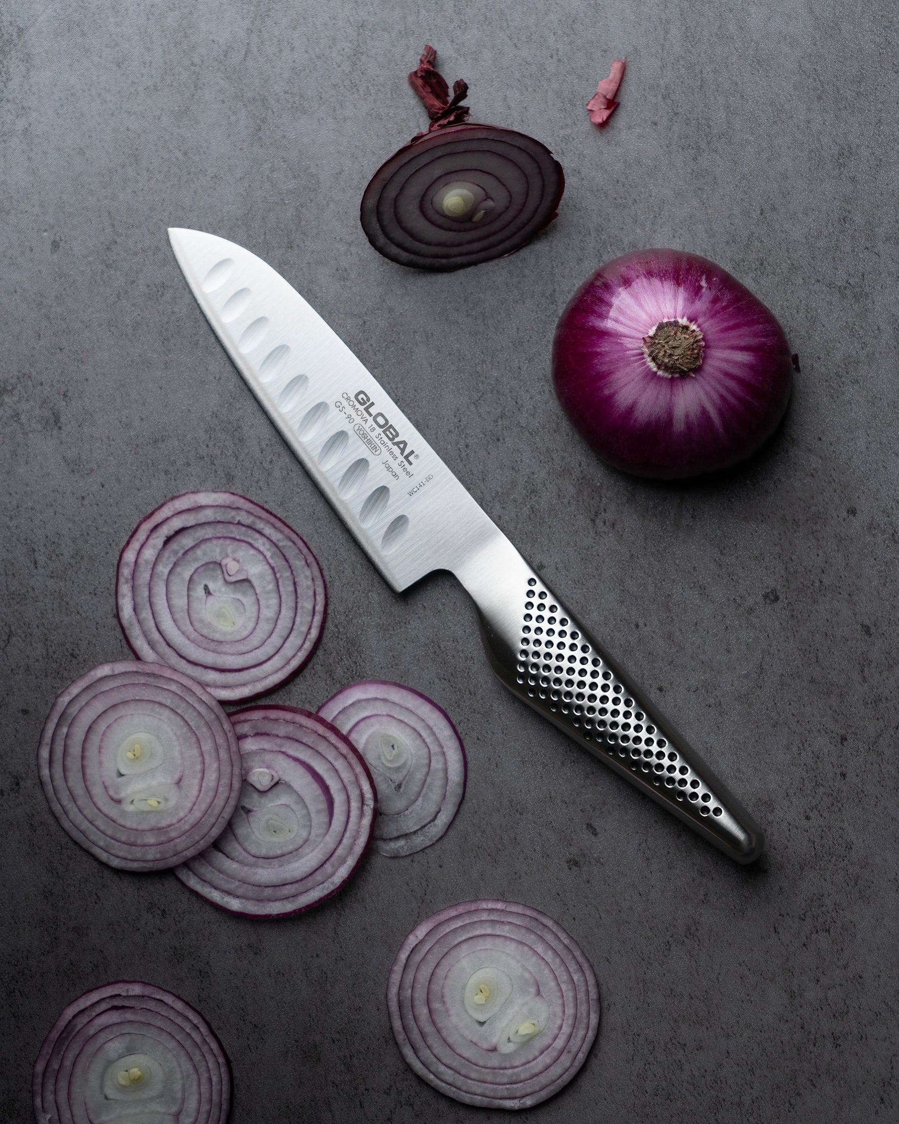 Global fluted santoku knife. Sliced red onions and a Global chef's knife on a gray surface
