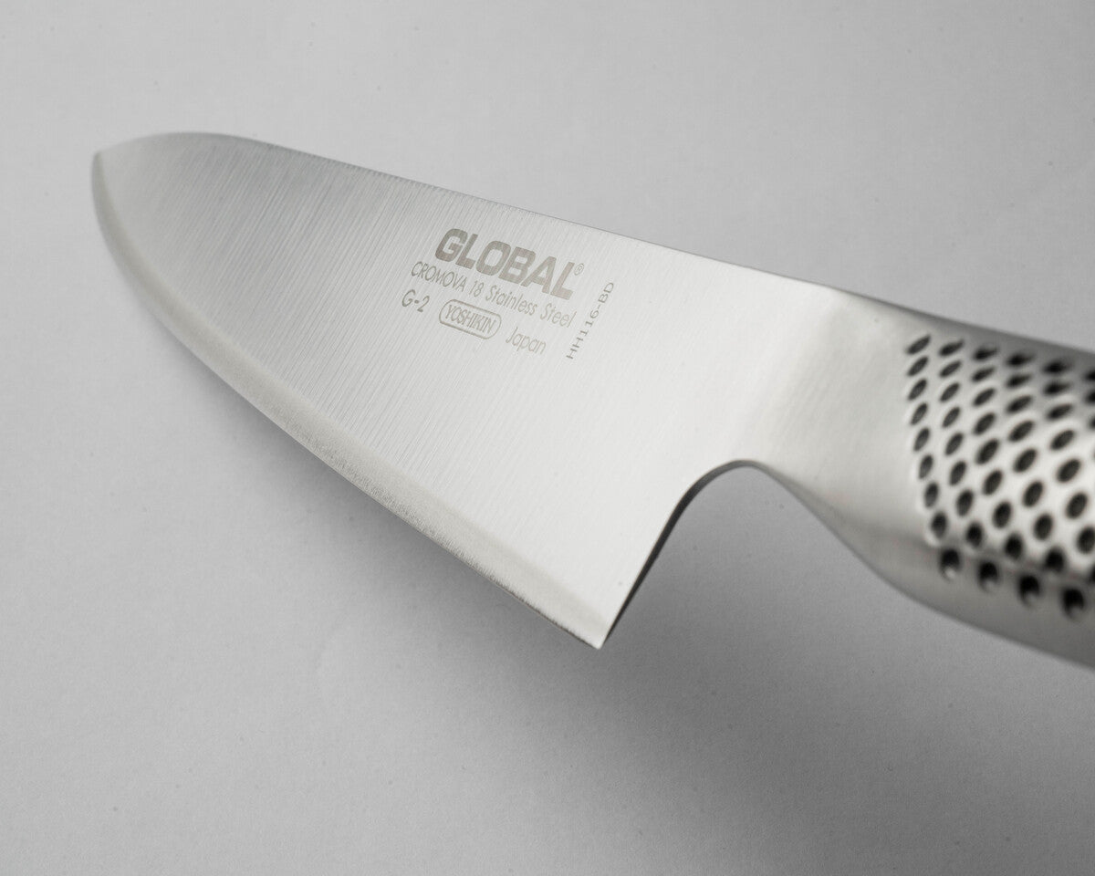 Close-up of a Global G-2 chef's knife blade on a light grey background. Global G-2 Cook's knife's ultra sharp blade with 15 degree cutting edge with global branding made form Cromova 18 stainless steel.