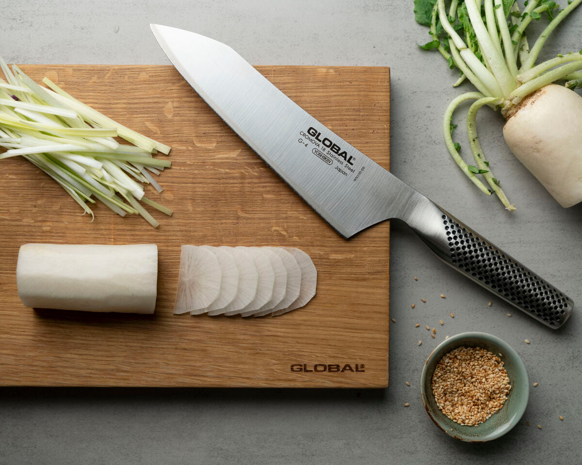 Global G-4 Japanese Chef's knife on a wooden cutting board with sliced vegetables and a bowl of spices.