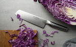 Global Japanese vegetable chopping knife on a cutting board with shredded purple cabbage on a grey surface