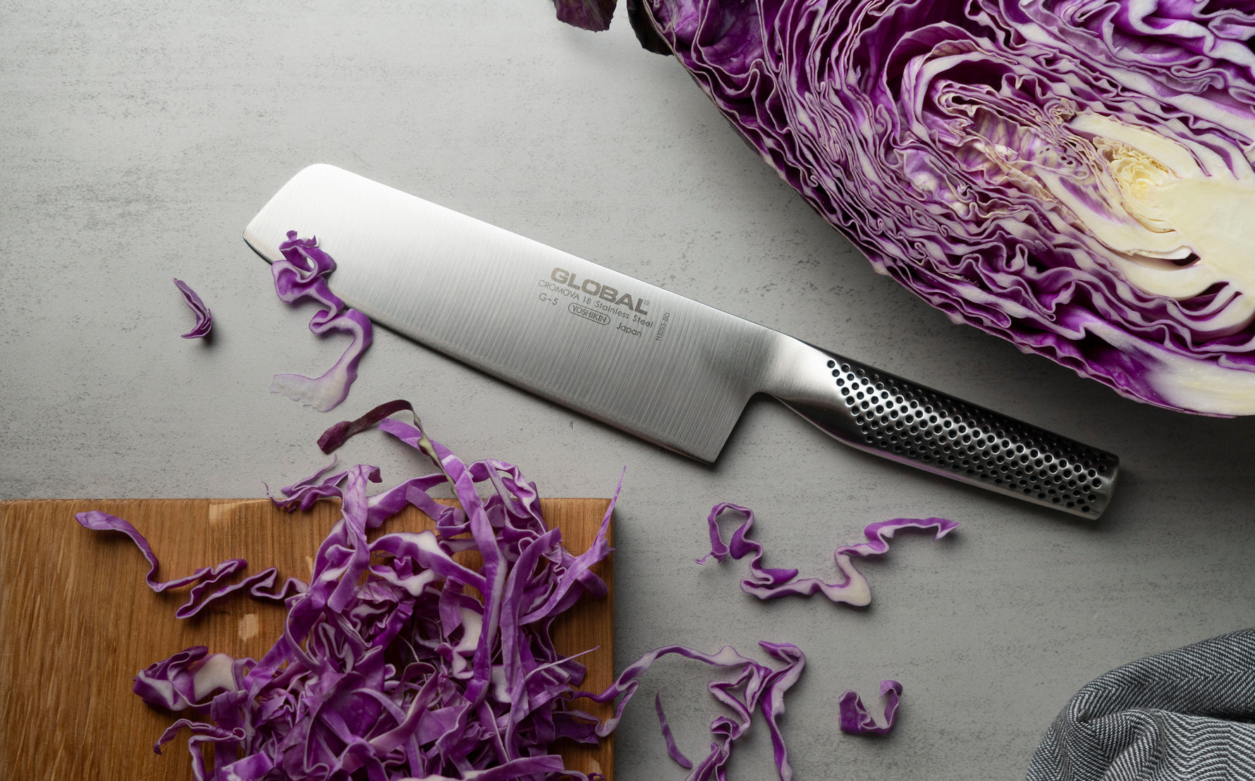 Global Japanese vegetable chopping knife on a cutting board with shredded purple cabbage on a grey surface