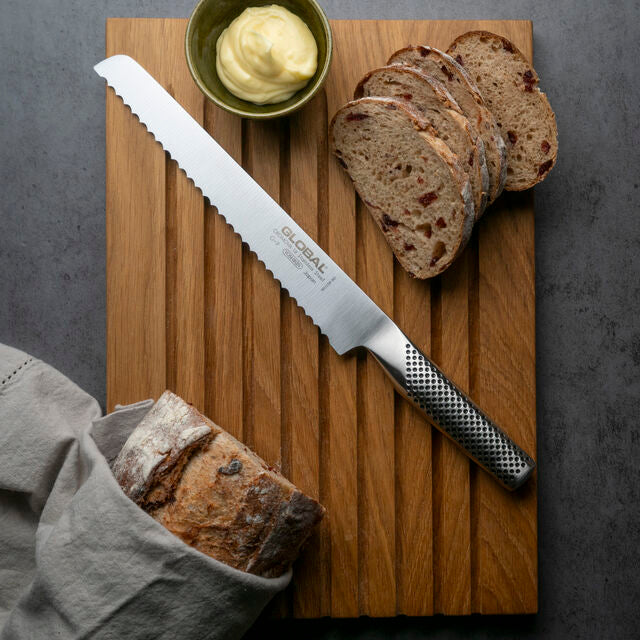 Serrated bread knife, the Global G-9 bread knife, on a wooden cutting board with sliced bread and butter.