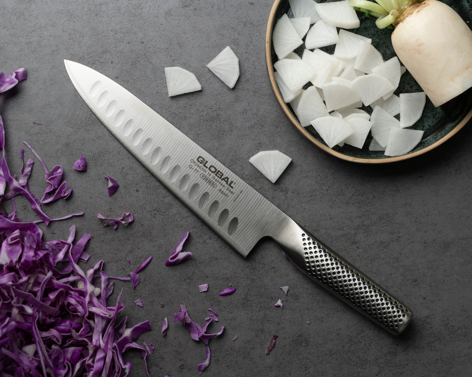 20cm Chef's knife with a branded handle on a dark surface with chopped vegetables. Global fluted chef's knife.