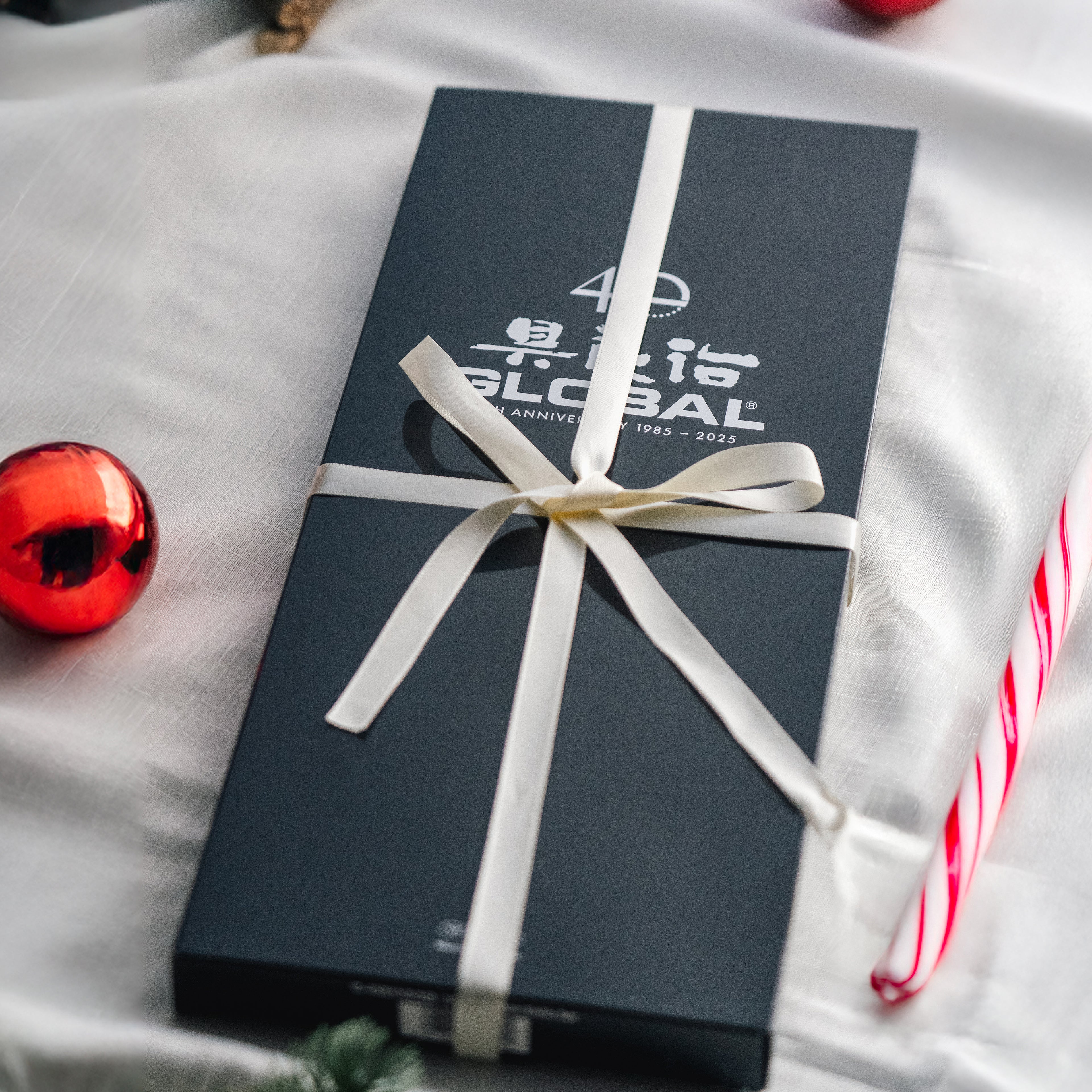 Black Global gift box with a white ribbon on a light grey fabric surface with Christmas decorations.