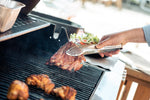 Home cook grilling meat on a barbecue with a stainless steel grilling tongs