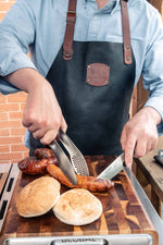 Barbecue chef using Global stainless steel kitchen tongs and kitchen knife wearing global leather apron.