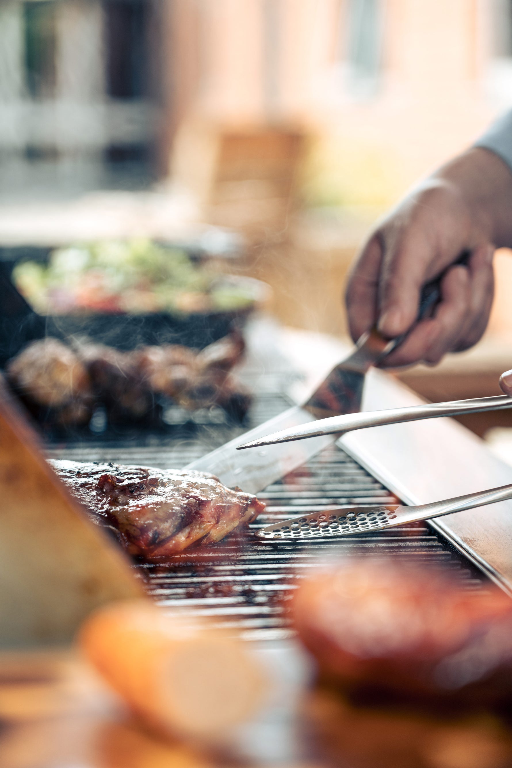 Bbq chef grilling meat on a barbecue  using stainless steel barbecue utensils with a blurred background.