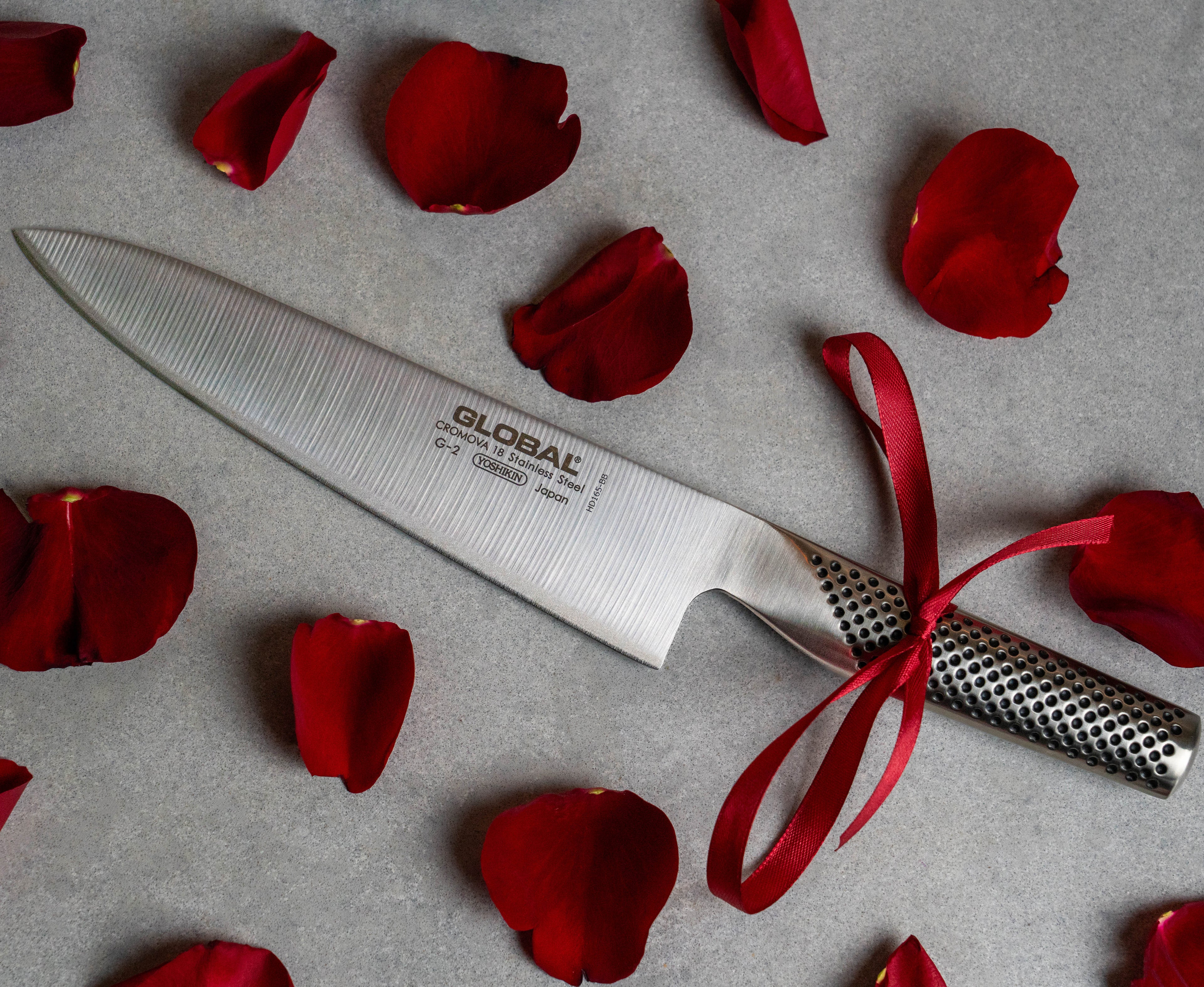 Global G-2 Chef's knife. Stainless steel kitchen knife next to rose petals gift wrapped with red ribbon for Valentines Day Gift. Gift idea for professional chefs and home cooks.